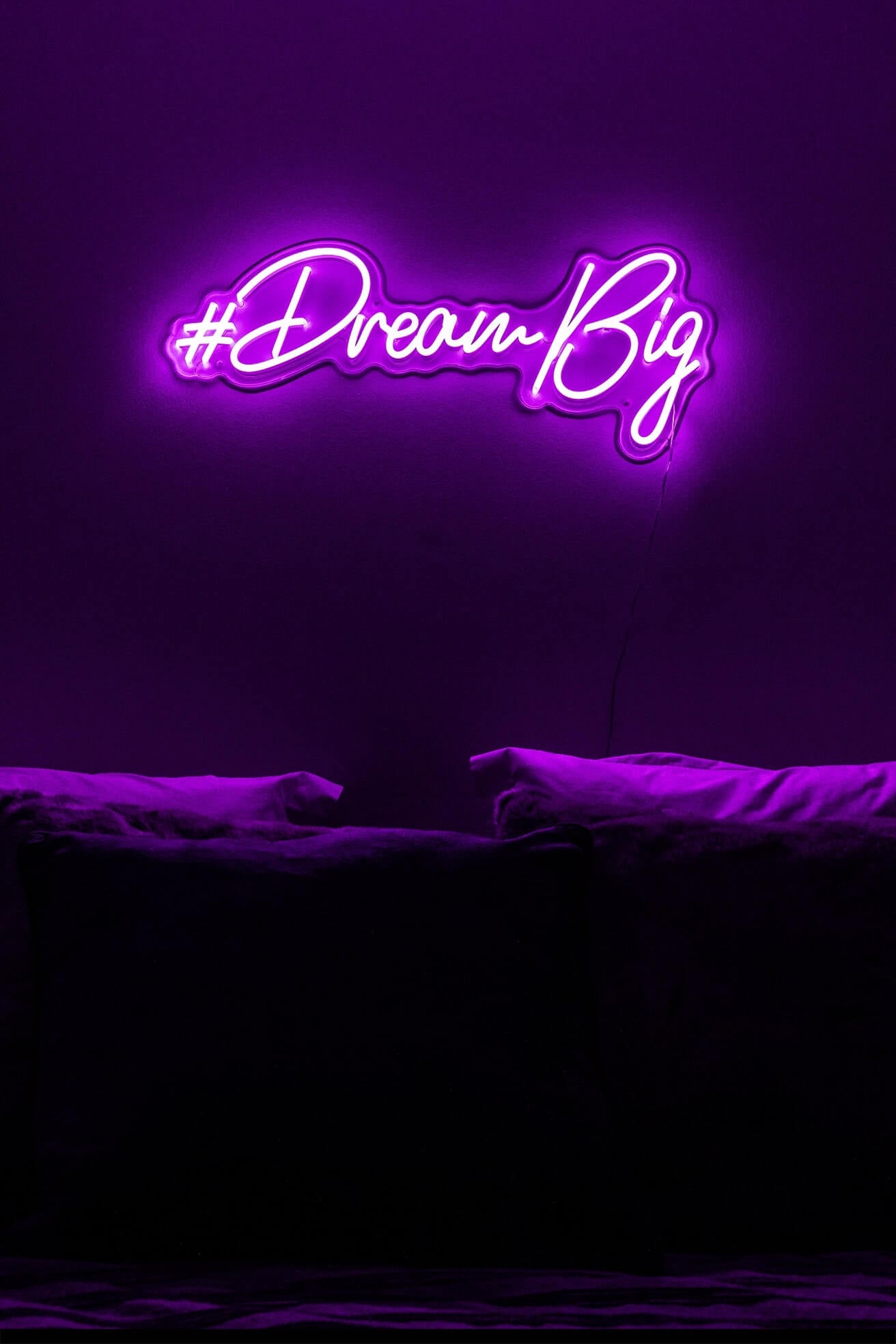purple dream big neon sign hanging on bedroom wall above bed