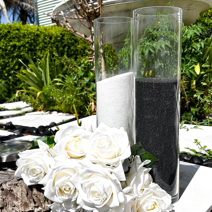 black and white sand candles placed on white stepping stones in garden bed with white roses