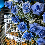 blue real touch roses and baby's breath hanging on white mesh backdrop with neon sign
