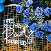 blue rose and baby's breath flower arrangement hanging on white mesh backdrop with white neon sign