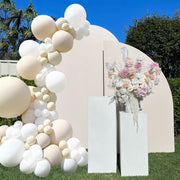 beige and white balloons hanging on beige arch backdrop with white plinths and colourful flower arrangement