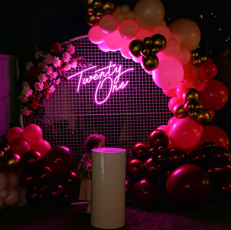 hot pink twenty one neon sign hanging on white circle mesh backdrop with balloons and plinth