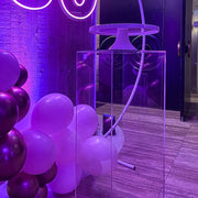clear plinth standing on floor with white cake stand on top and balloons behind