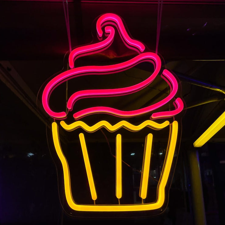 pink and yellow cupcake neon sign hanging on marquee at outdoor event