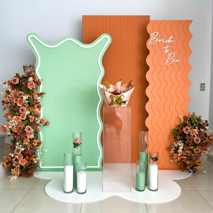 green and apricot coloured backdrop boards with terracotta flowers, clear plinth and sand candles
