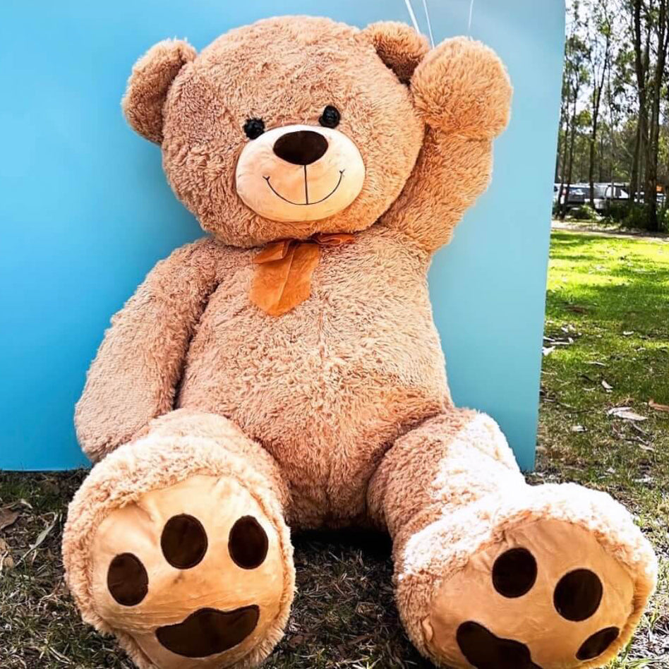 giant teddy bear sitting on grass against blue backdrop at park