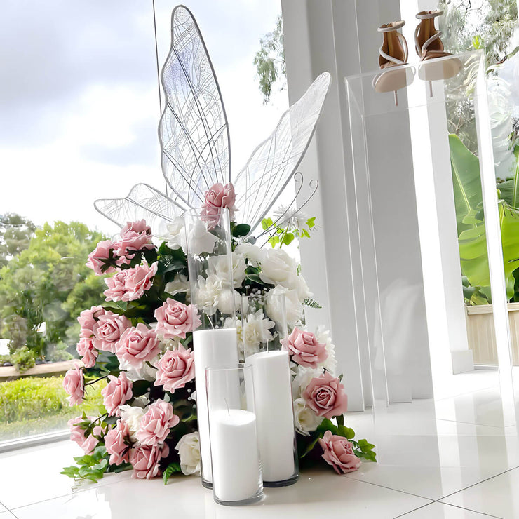 white led butterfly sitting on top of pink and white rose flower arrangement with white sand candles