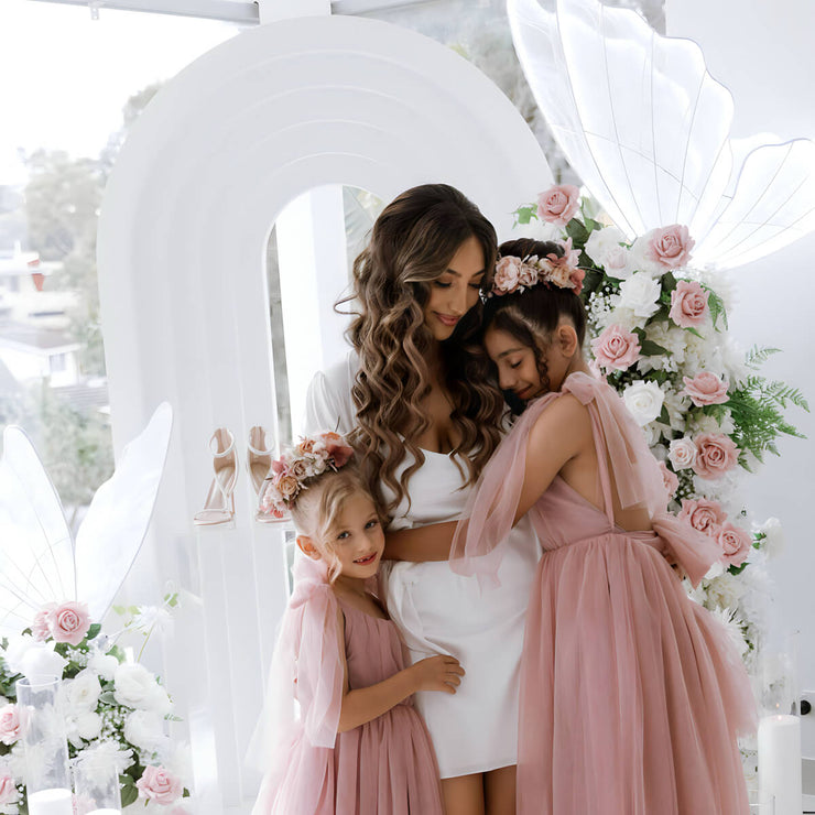 bride in white dress hugging flower girls in blush pink dresses on wedding day