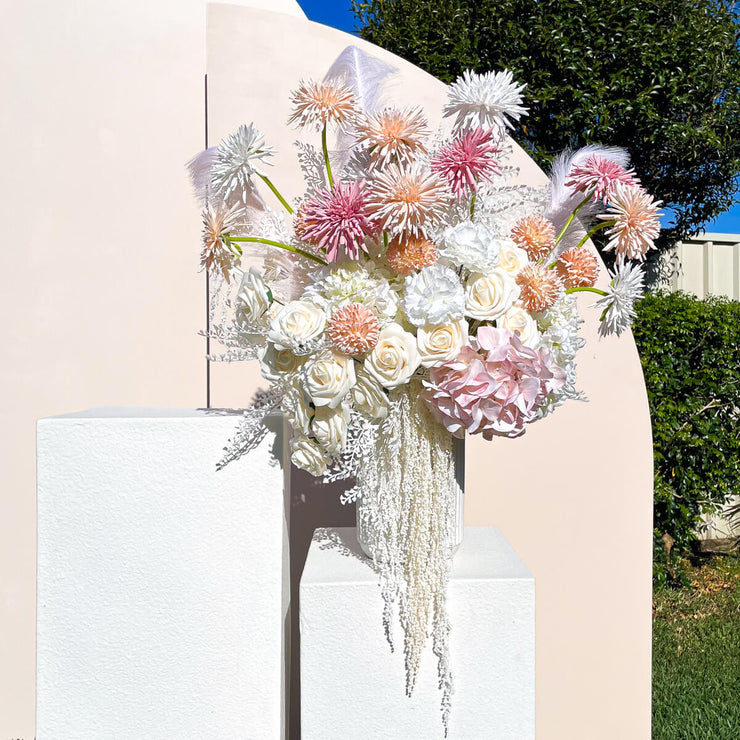 colourful boho themed flower arrangement standing on white plinth against beige arch backdrops