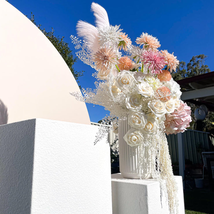 colourful pink, orange and white themed flower arrangement in white vase standing on white plinth