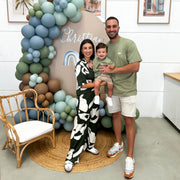 family with baby standing in front of brown arch backdrop with balloons, arm chair and rug