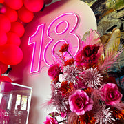 pink 18 neon sign hanging on beige arch backdrop with pink and gold flower arrangement