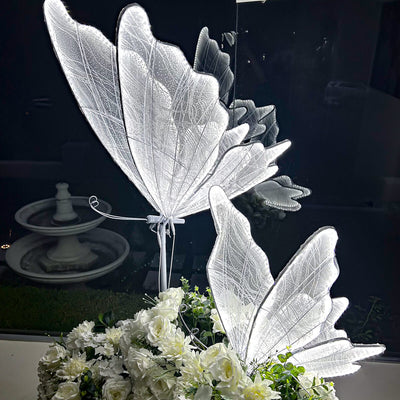 two white led butterflies standing up on top of white flower arrangement