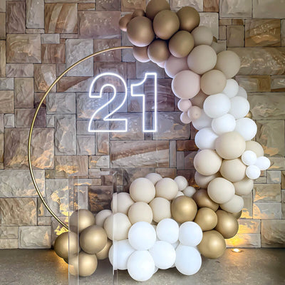 white 21 neon sign hanging on gold hoop backdrop with clear plinth and white and gold balloon arch