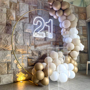 white 21 neon sign hanging on gold hoop backdrop with clear plinth and white and gold balloon garland arch