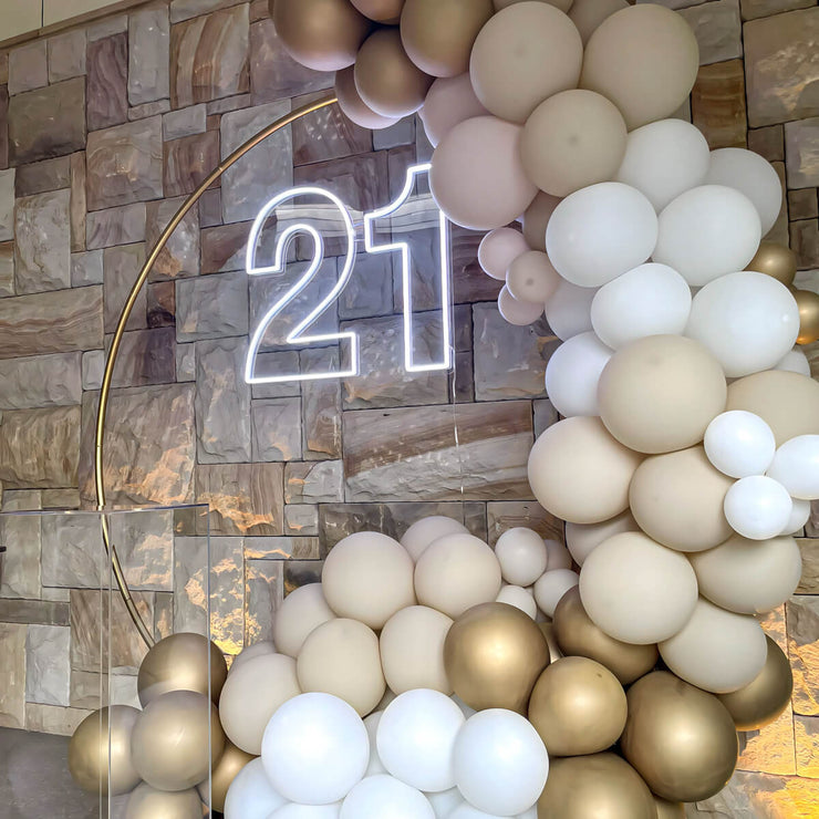 white 21 neon sign hanging on gold hoop backdrop with white and gold balloon arch against sandstone rock wall