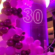 pink 30 neon sign hanging on white hoop backdrop with balloons and clear plinth