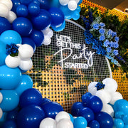 white let's get this party stated neon sign hanging on white circle mesh backdrop with blue flowers and blue and white balloons