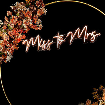 miss to mrs neon sign hanging inside gold circle backdrop with flower garland