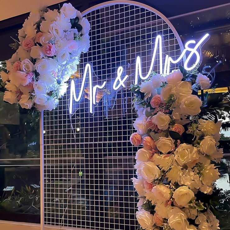 white mr and mrs neon sign hanging on white arch backdrop with white flower arrangement
