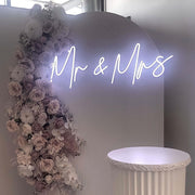 white mr and mrs neon sign hanging on white backdrop with white flower arrangement