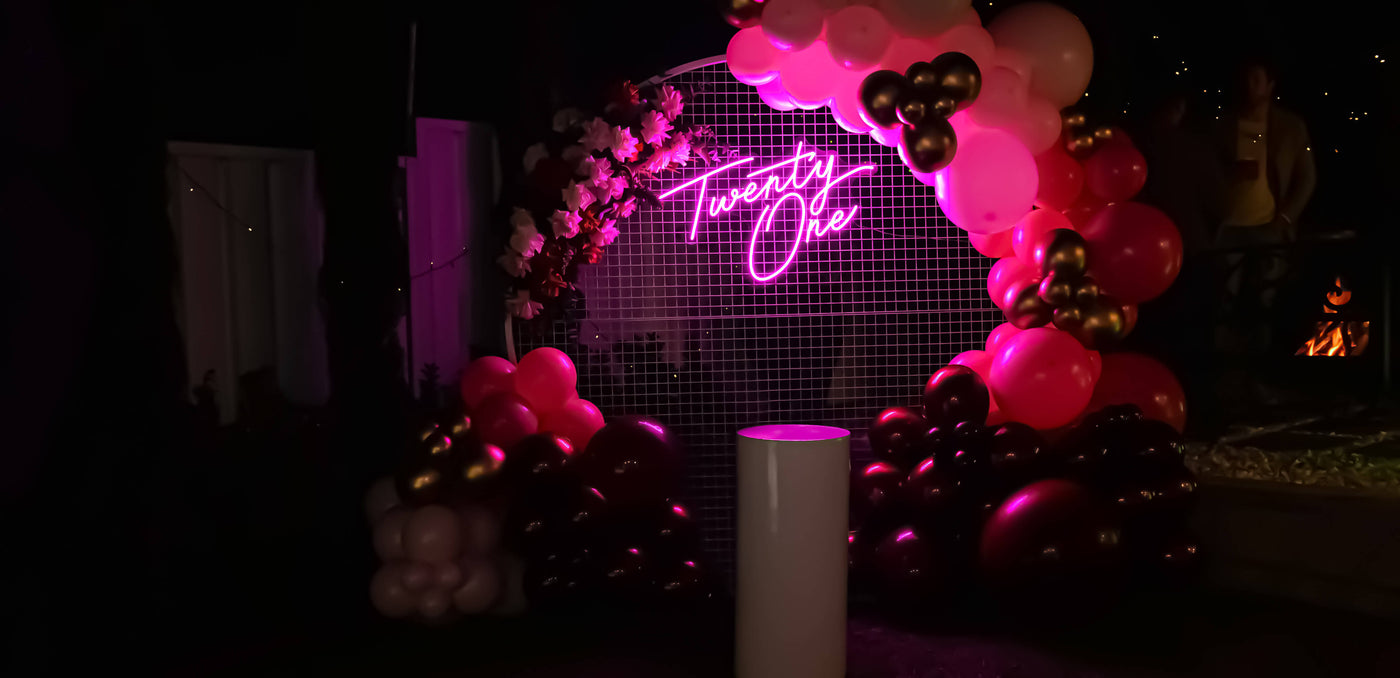 hot pink 21st birthday neon sign hanging on white backdrop with flowers and balloons