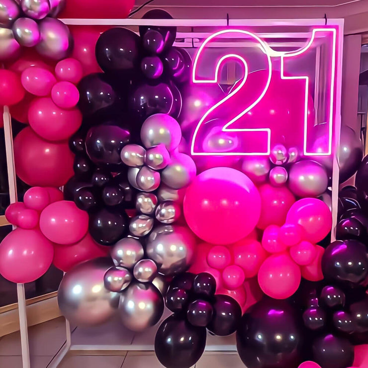 hot pink 21 neon sign hanging on frame with balloon backdrop