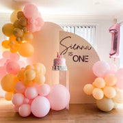 beige arch backrop setup with pink and peach balloons at child's first birthday
