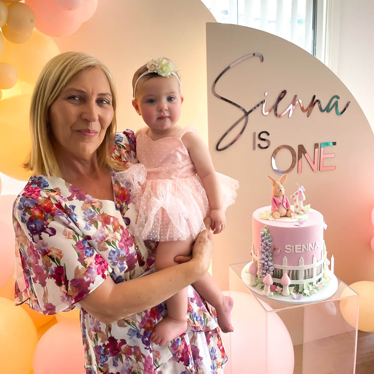 lady holding baby girl at her first birthday party with arch backdrops in background
