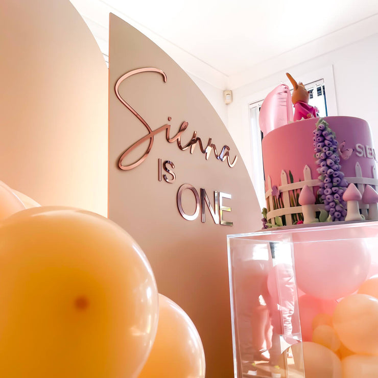 acrylic lettering stuck on beige sail backdrop with pink birthday cake and balloons