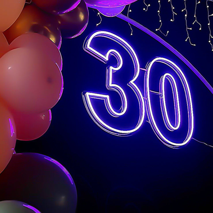 purple 30 neon sign hanging on white backdrop frame with balloons