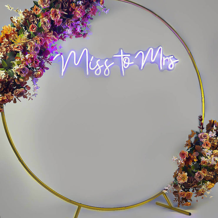 purple miss to mrs neon sign hanging inside gold circle backdrop with flower garland