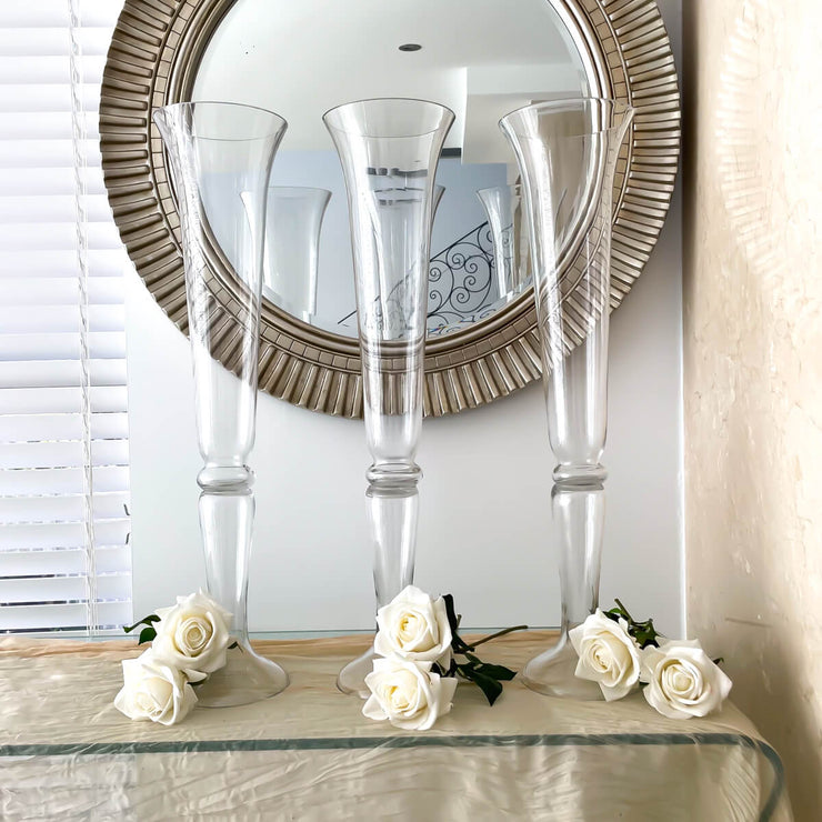 three tall glass vases standing on table with white roses at their feet