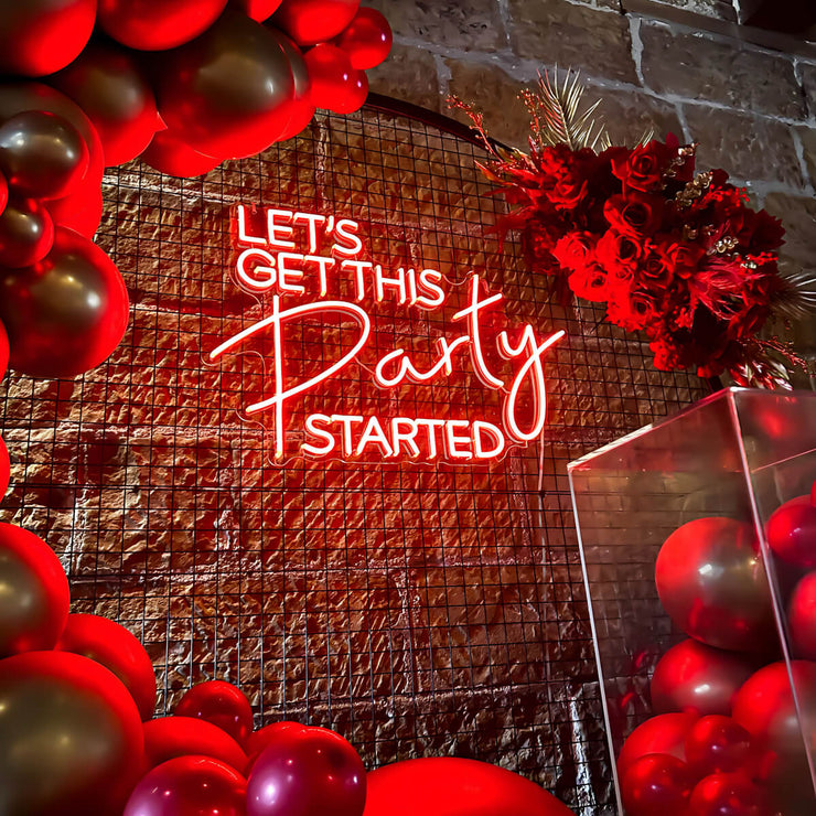 red lets get this party started neon sign hanging on black circle backdrop frame with plinth and flower arrangement