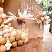 boho flower arrangement placed on top of clear plinths in front of beige backdrops at baptism event