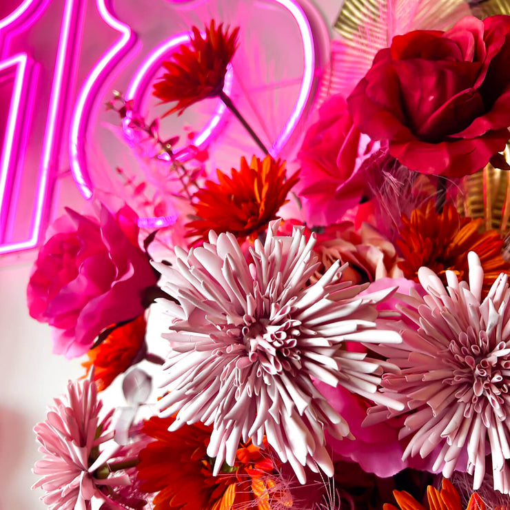 mix of bright pink, red and orange flowers with pink 18 neon sign in background