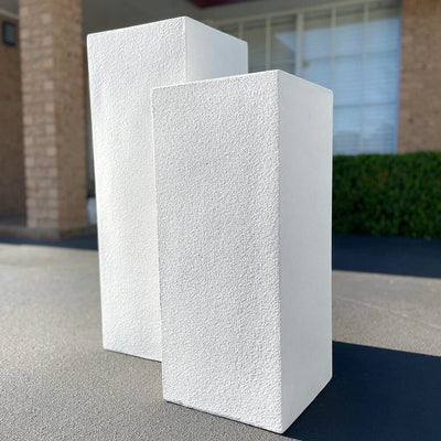 two off-white limestone plinths placed on floor with garden background