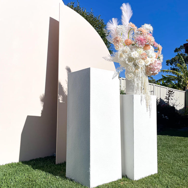 two textured white limestone plinths standing on grass in front of backdrops with flower arrangement