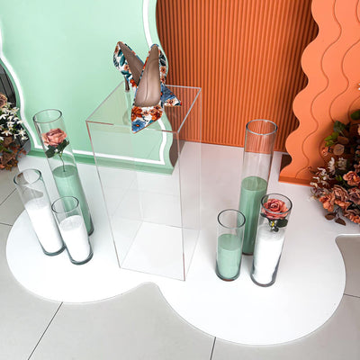 heels sitting on clear plinth with sand candles and green and orange backdrops