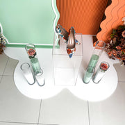 heels placed on clear plinth with green and white sand candles and white floor mat underneath