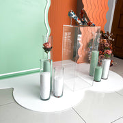 clear plinth and green and white sand candles standing on white floor mat