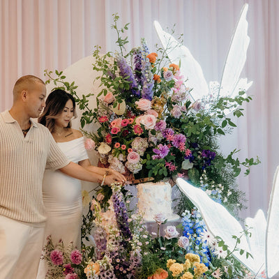 man and woman cutting cake amongst flowers and white led butterflies