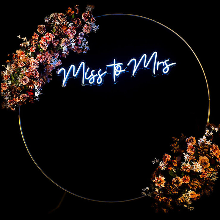 white miss to mrs neon sign hanging inside gold circle backdrop with flower garland