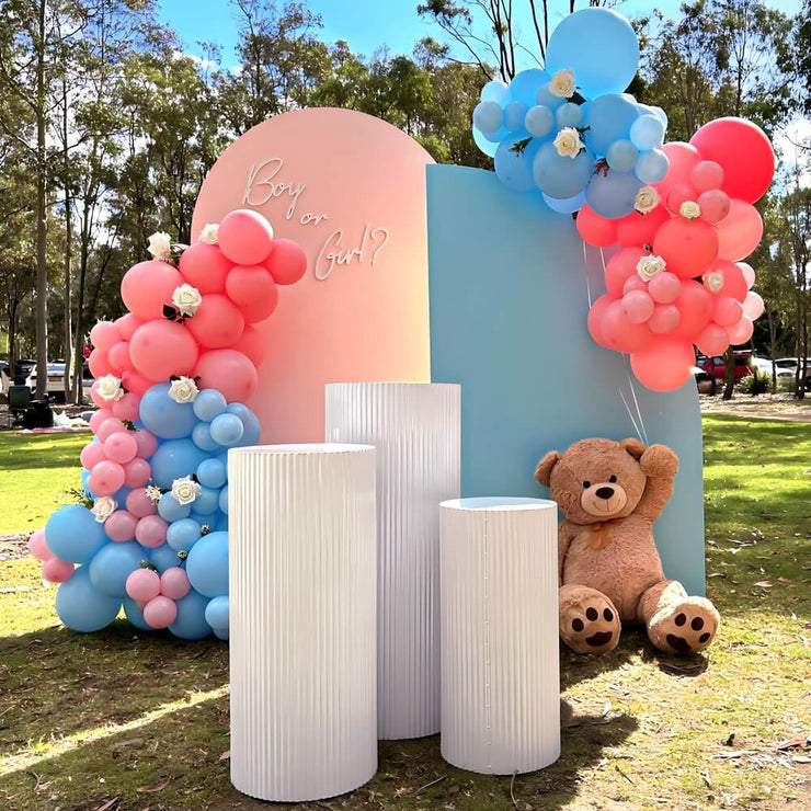 three white ripple plinths at park in front of pink and blue backdrops at gender reveal party