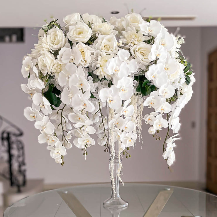 white rose and white orchid wedding arrangement in vase sitting on glass table
