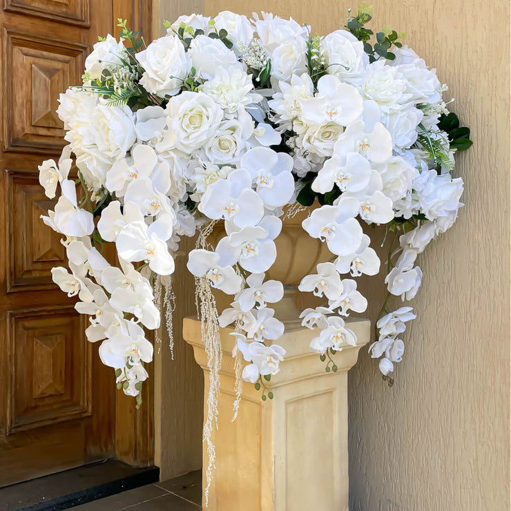 white rose and white orchid wedding arrangement placed on pillar outside house