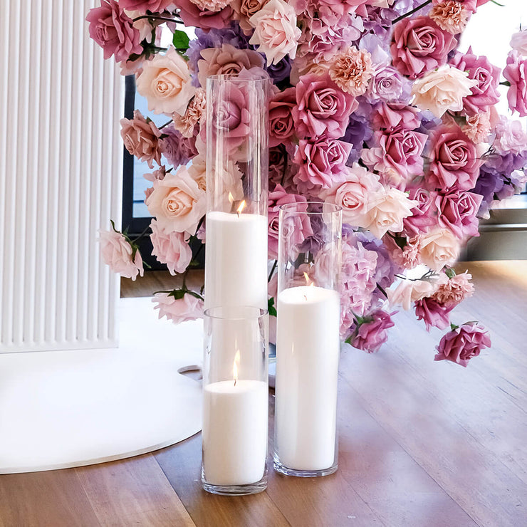 white sand candles in clear glass vases in front of dusty pink and white rose flower arrangement