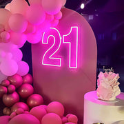 pink 21st birthday neon sign on backdrop with balloons