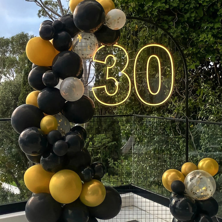 yellow 30 neon sign hanging on black backdrop frame with balloons