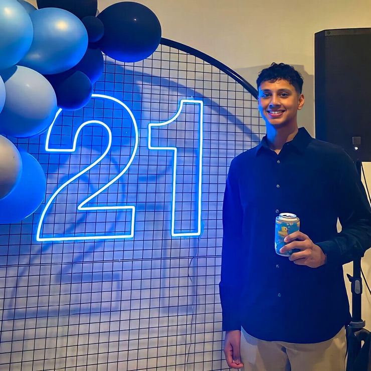 boy standing in front of blue 21 neon sign with balloon backdrop